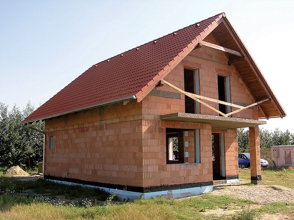 Stavba tehlového rodinného domu so sedlovou strechou.