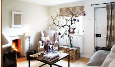 V obývacej izbe vo vianočnom období vyniká vyzdobená vetva jablone. Odtiene bielej, sivej a hnedej tu dopĺňa fialová, ktorá sa objavuje na jabloni aj na viacerých dekoráciách na konferenčnom stolíku.